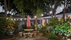 An outdoor patio area with a stone table and chairs, surrounded by potted plants and a string of lights. - Wilton Manors, Cute Outdoor Space-New Bathroom, Pool 3 (Wilton Manors)