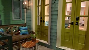 A green door with a number plate, a bench with cushions, and a small table with a plant. - Charming New Orleans Bungalow Steps from French Quarter (New Orleans)