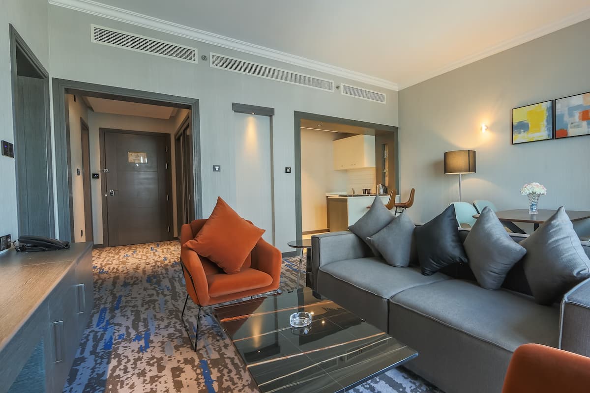 A modern hotel lobby with a sofa, armchairs, a glass coffee table, and a dining area.