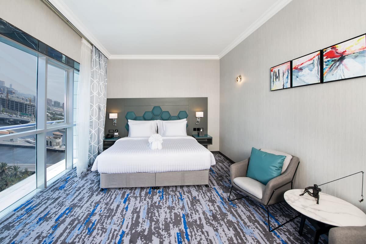 A hotel room with a large bed, a sofa, a small table, and a city view.