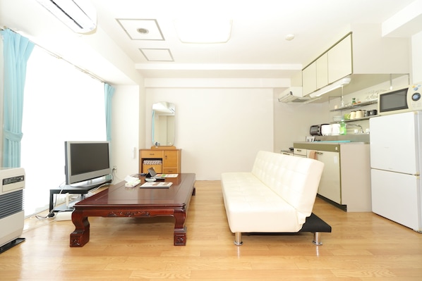 Un espacio habitable compacto con sofá, una mesa de centro de madera, televisión, y una pequeña cocina equipada con microondas y refrigerador.
