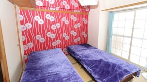 Ein Zimmer mit zwei Betten, einer roten Wand mit Muster und einem Fenster mit Vorhang.