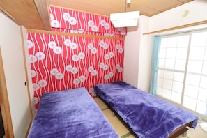 Una habitación con dos camas, una pared con diseño rojo y una ventana con cortina.