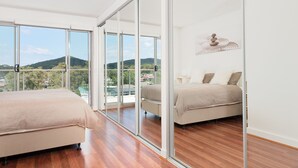 Quarto com uma grande porta de correr de vidro que dá para uma varanda, uma cama, uma mesinha de cabeceira e uma obra de arte pendurada na parede.