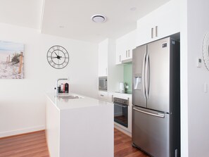 A modern kitchen with a stainless steel refrigerator, a built-in oven, and a coffee maker on the counter. - Shoal Bay Apt 501 Shoal Bay (Shoal Bay)