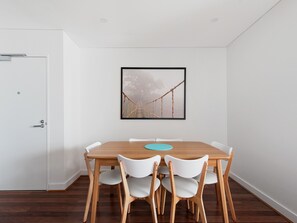 Ein Essbereich mit einem Holztisch, weißen Stühlen, einem gerahmten Bild an der Wand und einer weißen Tür.