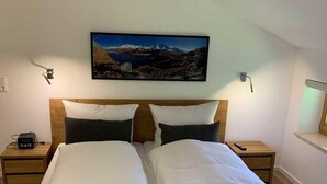 Una cama doble con estructura de madera, dos mesitas de noche, un cuadro colgado y un aparador con lámpara.