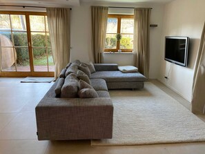 Una sala de estar con un sofá seccional, un televisor de pantalla plana y un ventanal con cortinas.