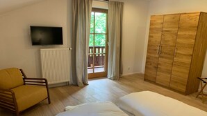 Un dormitorio con cama, una silla, armario, televisor y ventana con cortinas.