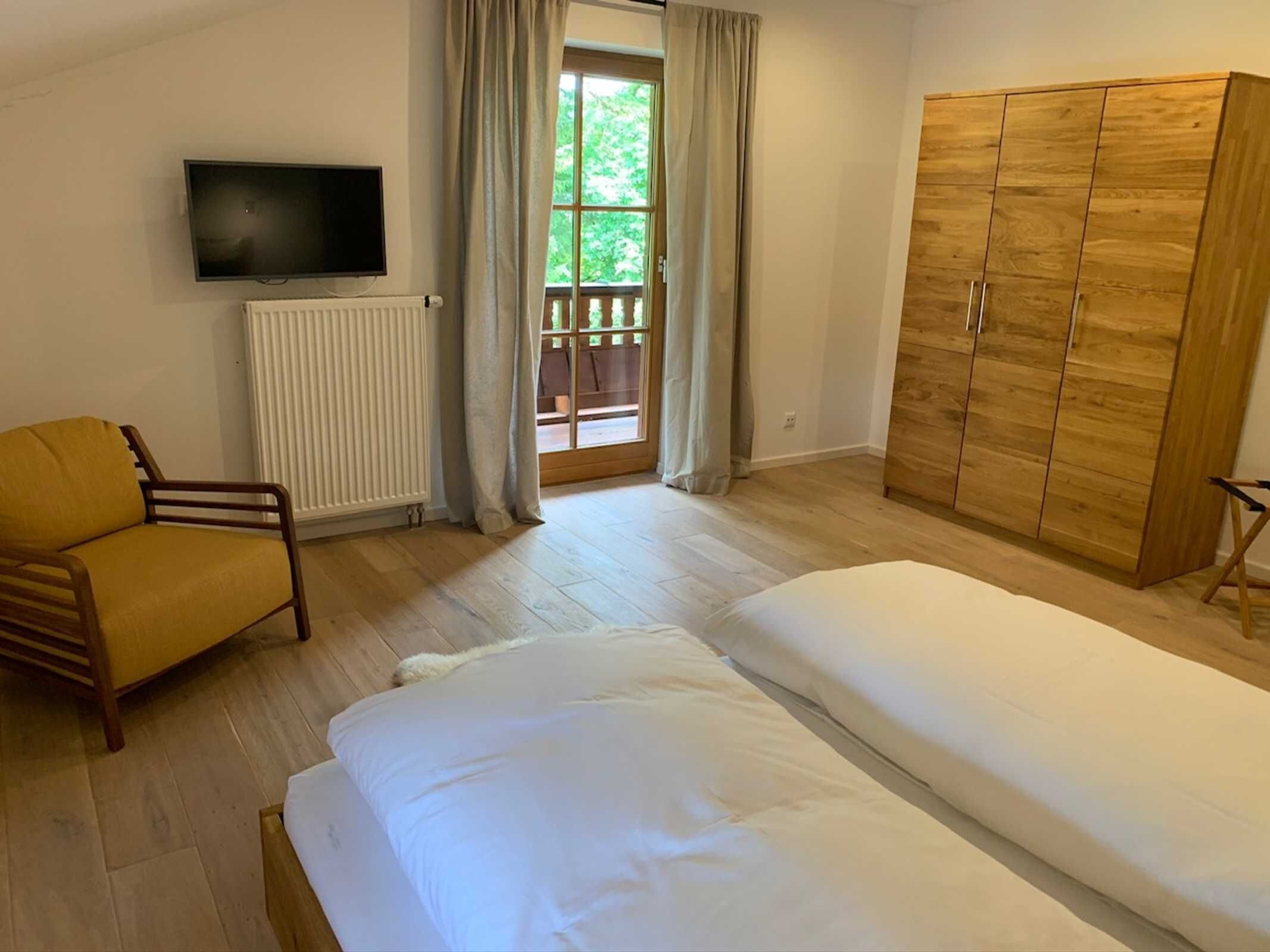 A bedroom with a bed, a chair, a wardrobe, a television, and a window with curtains.