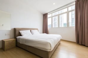 Ein Schlafzimmer mit Bett, Nachttisch, einem Fenster mit Vorhängen und Blick auf Gebäude.