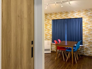 A room with a wooden door, a brick wall, a table with chairs, and a window with curtains. - PIER6 Otaru (Otaru)