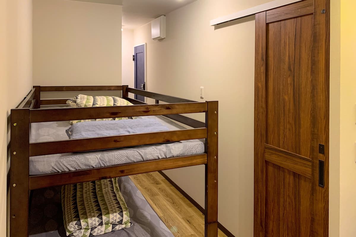 Una cama litera con tres niveles, una puerta de madera y un pasillo con una lámpara.