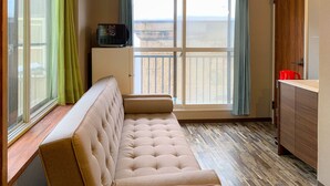 Ein Zimmer mit einem beigen Sofa, einer kleinen Kommode und Blick durch ein großes Fenster.