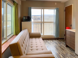 A room with a beige sofa, a small cabinet, and a view through a large window. - PIER6 Otaru (Otaru)