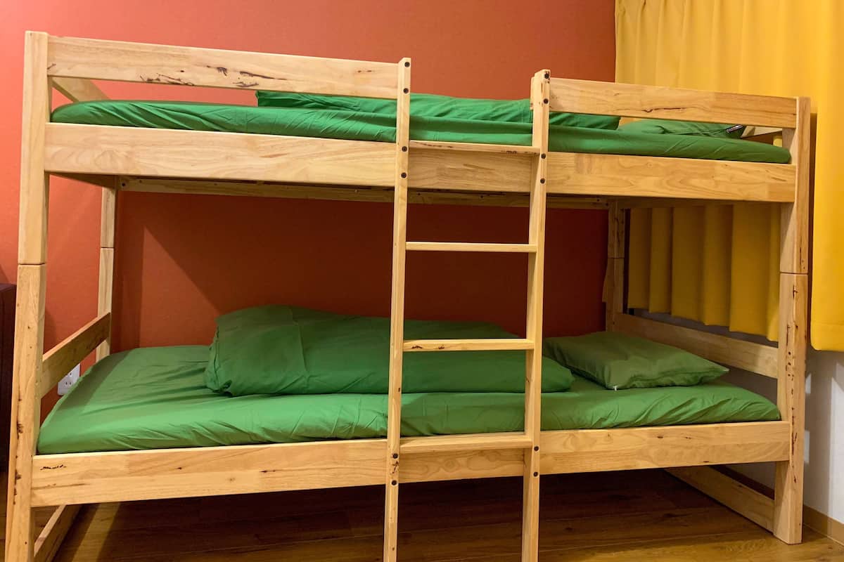 Una cama litera con escalera, ropa de cama verde y estructura de madera.