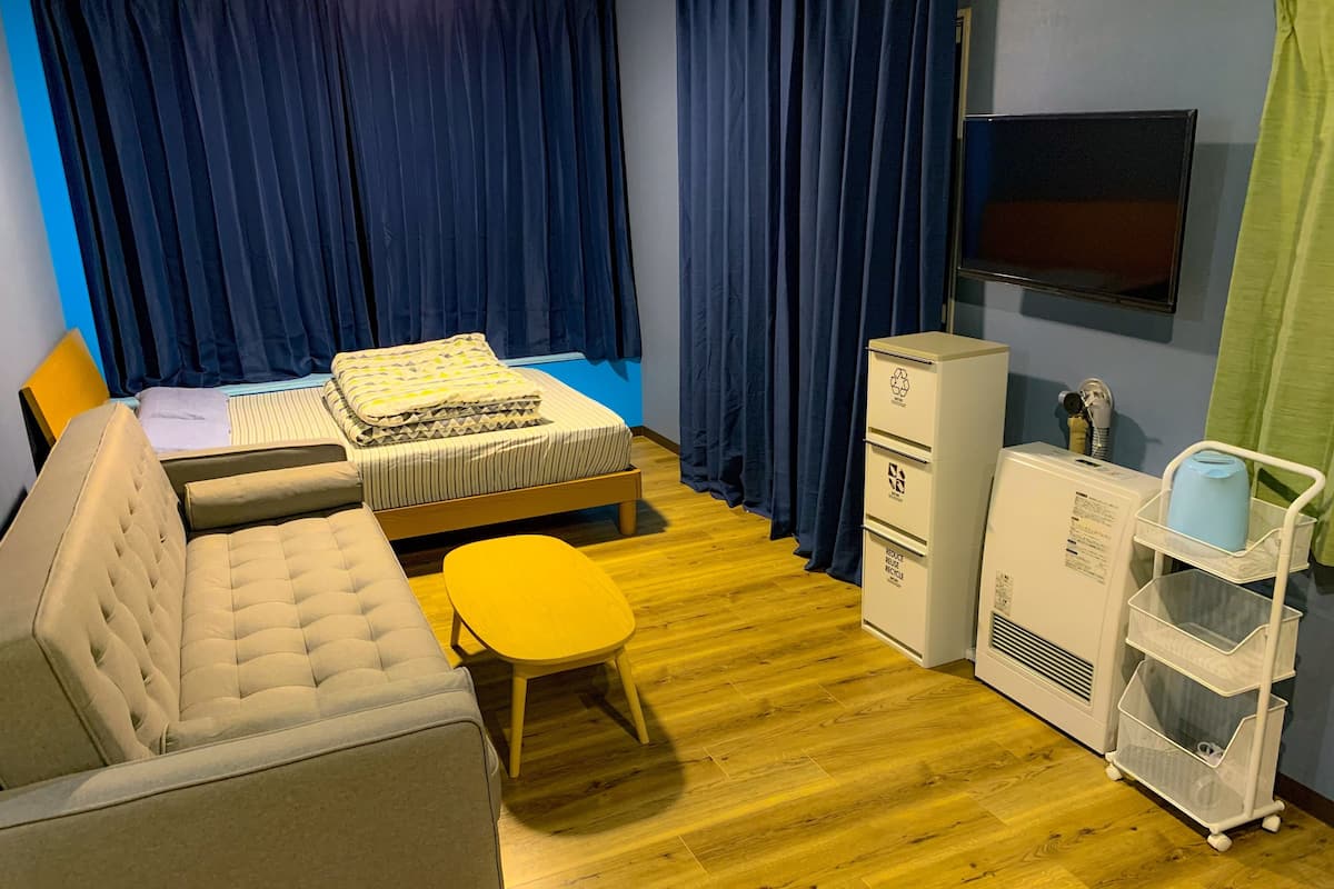 Una habitación de hotel con cama, sofá, una mesita, televisor, armario y contenedor de reciclaje.