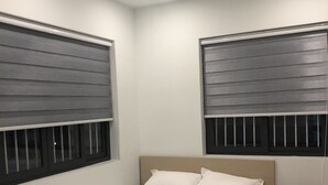 Ein Schlafzimmer mit einem Bett, zwei Fenstern mit Jalousien und einer Deckenleuchte.