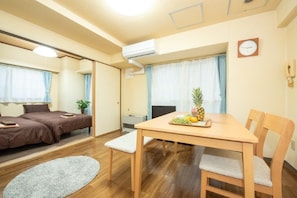 A compact hotel room with a bed, a dining table with chairs, a small rug, and a clock on the wall.