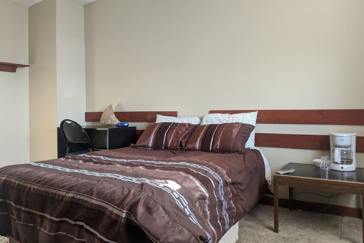 Habitación de hotel con cama, mesita de noche, silla y cafetera.