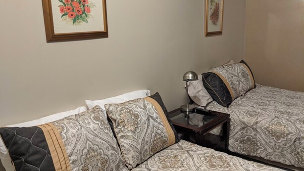 A hotel room with two beds, a nightstand, a lamp, and two framed floral paintings on the wall.