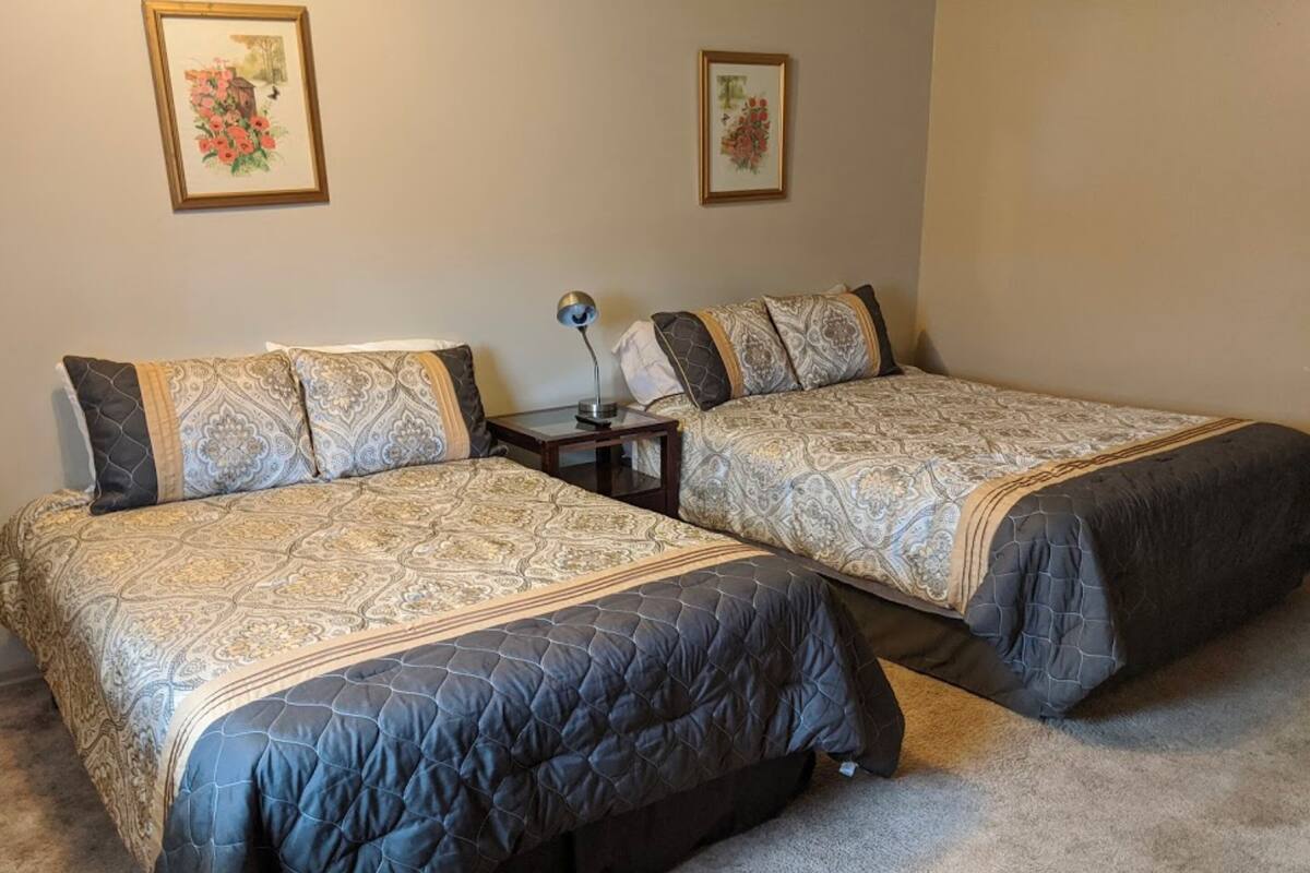 Dos camas dobles con ropa de cama estampada, una mesita de noche con lámpara y dos cuadros con motivos florales en la pared.