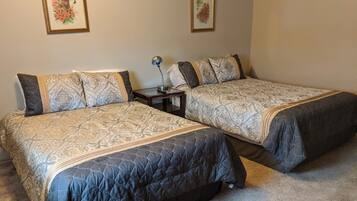 Two double beds with patterned bedding, a bedside table with a lamp, and two framed floral artworks on the wall.