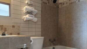 A bathroom with a toilet, bathtub, and a towel rack with multiple towels.
