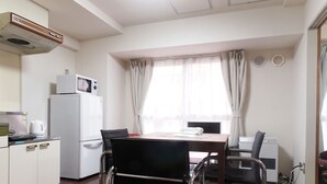 Una cocina compacta equipada con refrigerador, microondas y tetera. Cuenta con una mesa de comedor con sillas y un ventanal con cortinas.