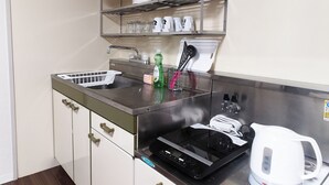 Una cocina compacta con un lavamanos, una tetera, un escurreplatos y una estantería con platos y tazas.