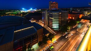 Paesaggio urbano notturno con edifici illuminati, uno stadio e un hotel moderno a più piani.
