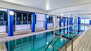 Una piscina interna con pareti di vetro trasparenti, pilastri blu e pavimento piastrellato.