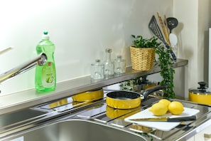 A kitchen with a stainless steel sink, a yellow pot, lemons, and a bottle of apple vinegar.