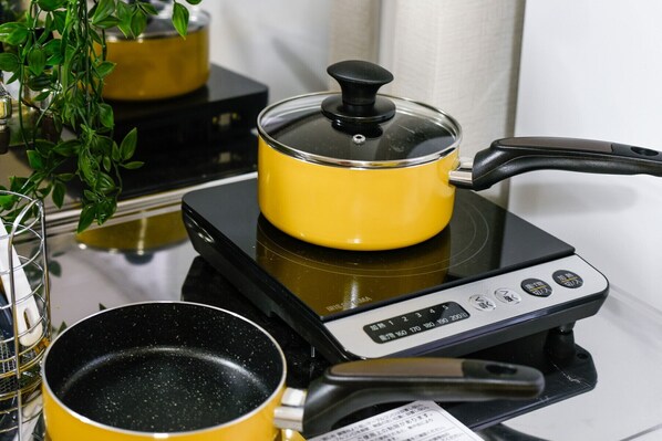 A portable electric stove with a yellow pot on it, a black pan, and a glass container.