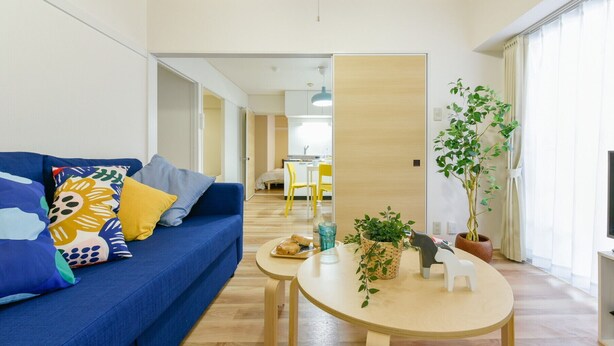 A modern living room with a blue sofa, a round wooden table, and a potted plant. - Heights Showa 207 (Sapporo)