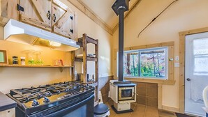 Una cocina con estufa a gas, estufa de leña y ventana con vistas a árboles.