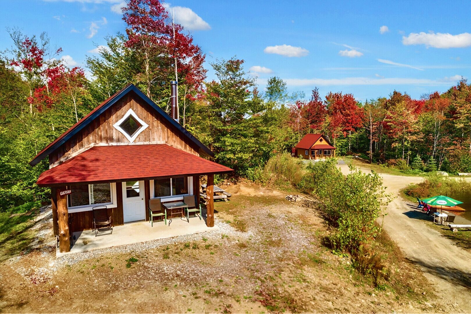 Une cabane en bois avec un toit rouge, une véranda avec des chaises et une petite table.