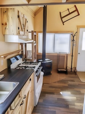 Una cocina con estufa a gas, armarios de madera y una ventana con persianas.