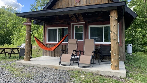 Une cabane en bois avec une véranda, deux fauteuils inclinables, un hamac et une table de pique-nique.
