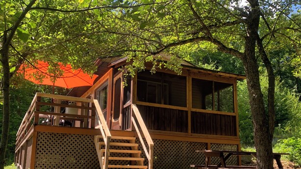 A wooden cabin with a balcony, a staircase, and a picnic table.