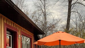A wooden deck with a table and chairs, a red door, and an orange umbrella.