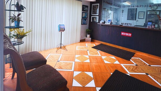 A reception area with a check-in counter, a seating area with a patterned floor, and a wall with framed pictures and a sign. - Huntington Suites (Huntington Beach)