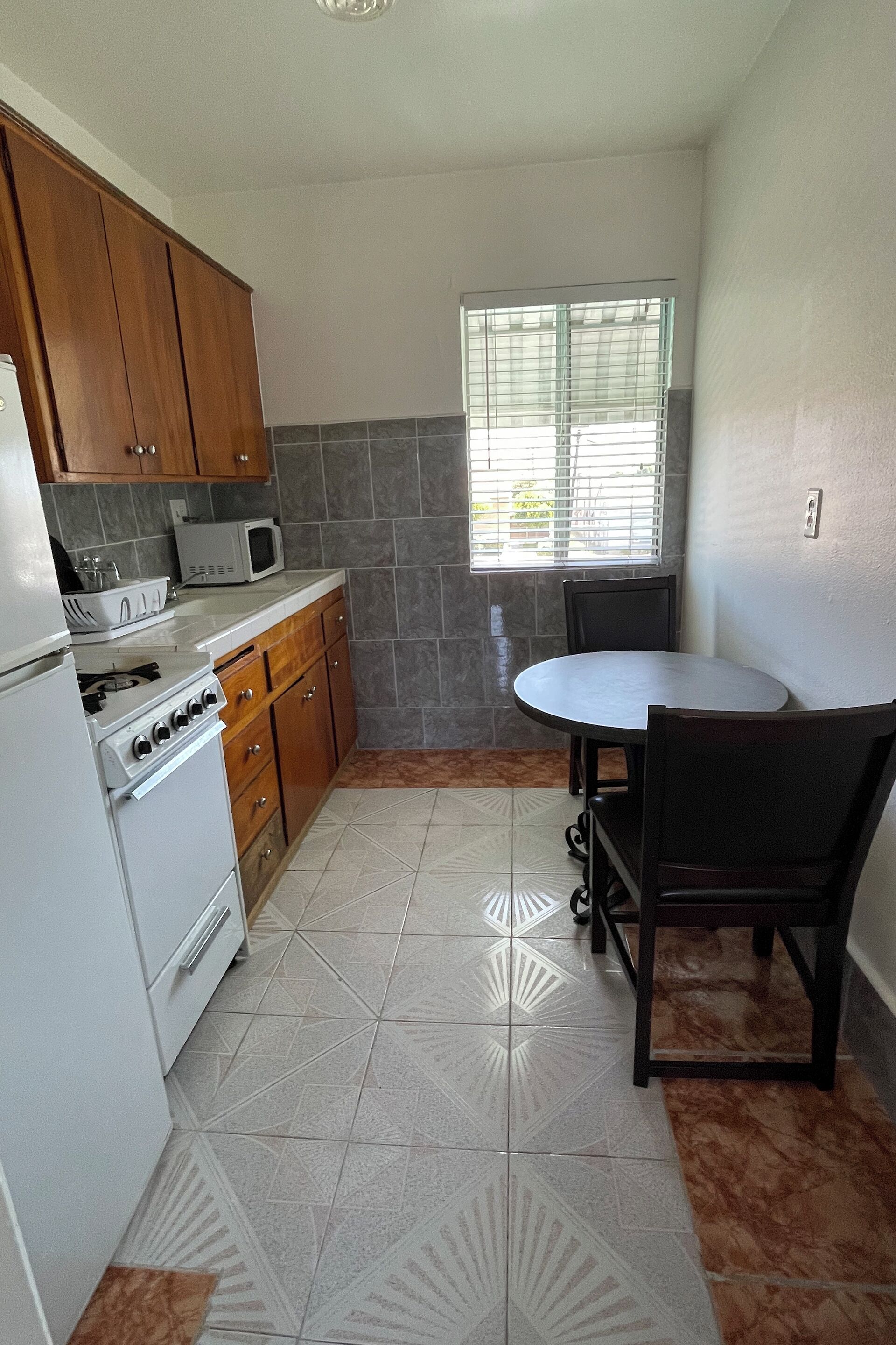 Cocina compacta con estufa, microondas y armarios. Hay una mesa de comedor con sillas y una ventana con persianas.