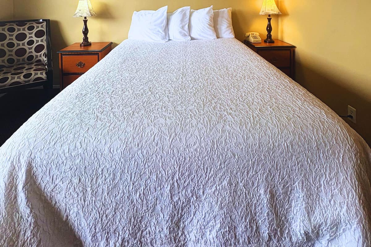 Een hotelkamer met een groot bed, twee nachtkastjes met lampen, een stoel en een schilderij aan de muur.