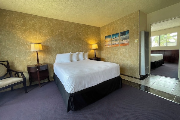 Una habitación de hotel con una cama grande, dos mesitas de noche con lámparas, una silla y un cuadro en la pared.