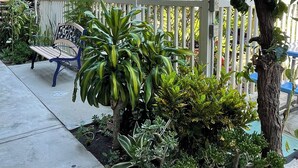 A courtyard with a white picket fence, a bench, and various plants. - Huntington Suites (Huntington Beach)