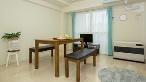 A small, well-lit room with a wooden table, two benches, a TV, and a window with curtains. - Heights Showa 503 (Sapporo)