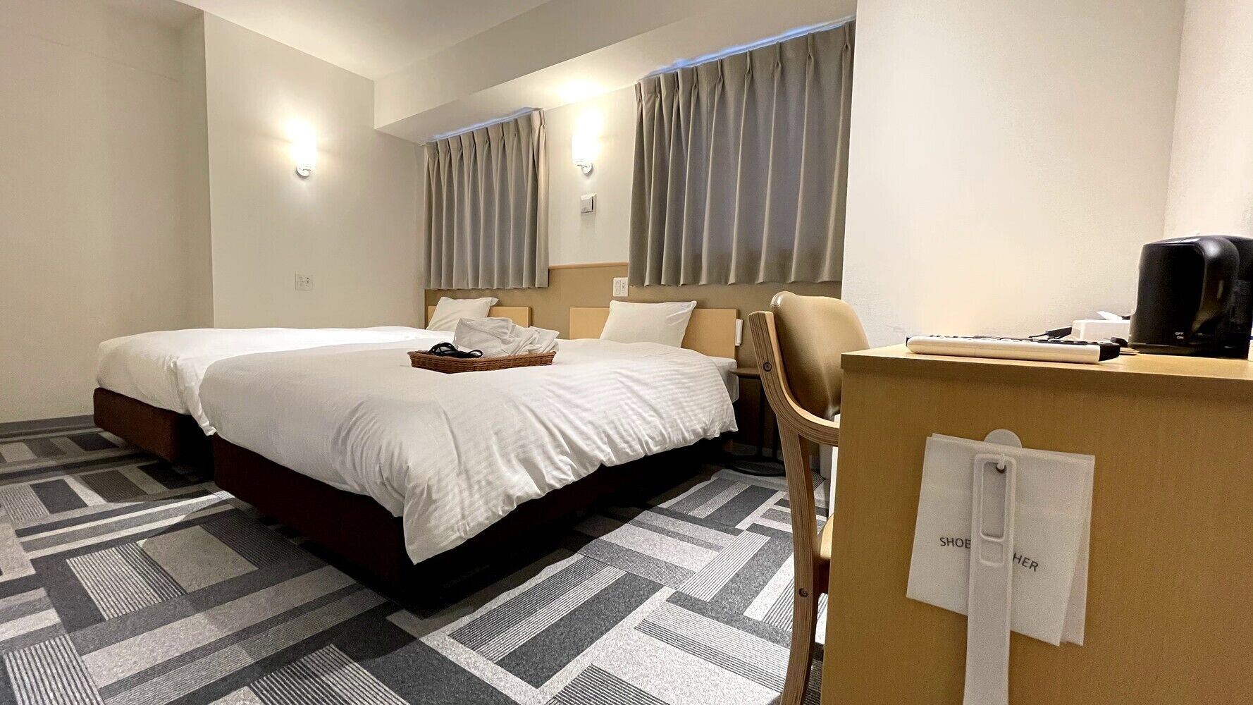 Quarto de hotel com duas camas, uma escrivaninha, uma cadeira e uma máquina de café.