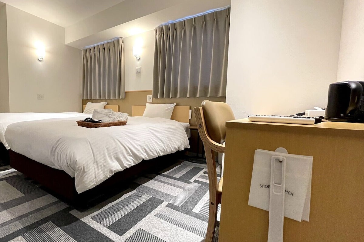 A hotel room with two beds, a desk, a chair, and a coffee machine.
