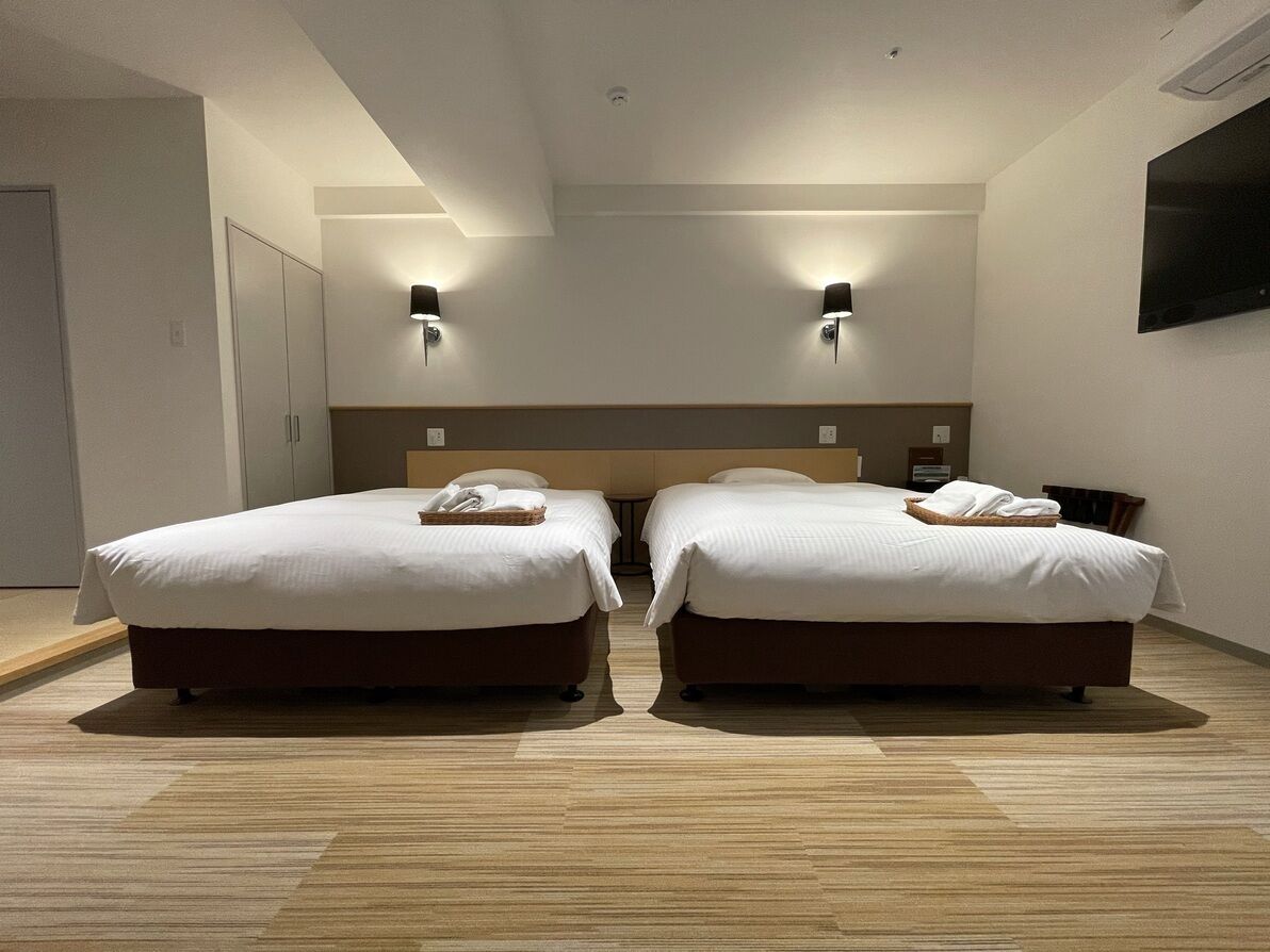 Quarto de hotel com duas camas, piso de madeira, cabeceira, luminárias fixadas na parede e televisão de tela plana.